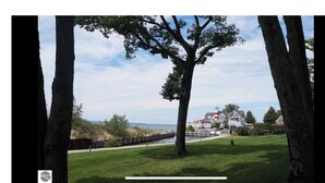 A coastal property with a large tree, a grassy lawn, and a house with a red roof and white walls.