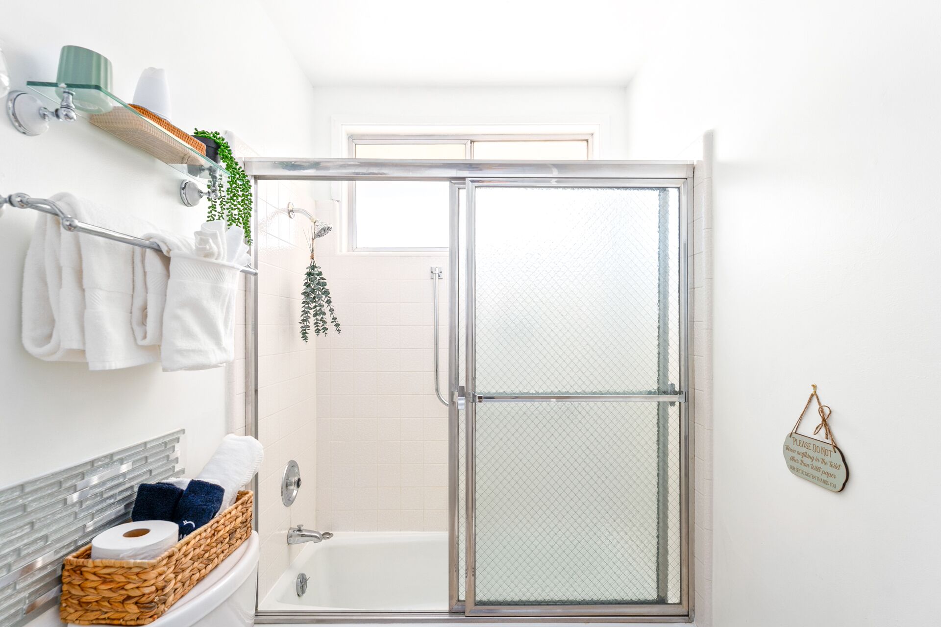 Une salle de bain moderne avec une douche à parois de verre, des toilettes avec un panier contenant des articles de toilette et un porte-serviettes avec des serviettes blanches.