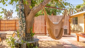 Una cadira espanyola penjada d'un arbre a un pati darrere amb una tanca de fusta, un barbacoa i una taula de pati.