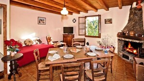 A cozy dining area with a wooden table set for four, surrounded by wicker chairs. A fireplace with a stone facade is visible to the right.
