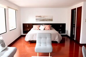 A bedroom with a bed, a chair, a bedside table, and a wall-mounted artwork.