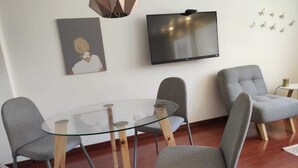 Een moderne vergaderruimte met een glazen tafel, grijs gestoffeerde stoelen, een flatscreen-televisie en een aan de muur bevestigd kunstwerk.