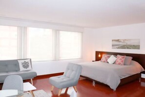 A modern bedroom with a bed, a grey sofa, a chair, and a painting on the wall.