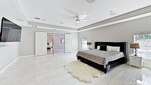 A spacious bedroom with a large bed, a ceiling fan, and a television on the wall.