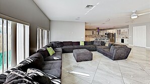 A spacious living area with a large L-shaped sectional sofa, a small ottoman, and a dining area in the background.