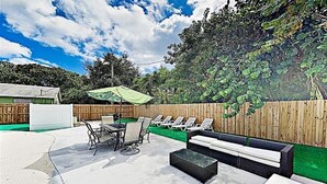 An outdoor patio with a table and chairs, a sofa, and a covered area with a green umbrella.
