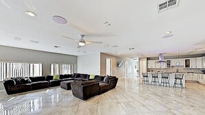 A spacious living area with a sectional sofa, a ceiling fan, and a kitchen area with bar stools.