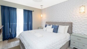 A bedroom with a large bed, a ceiling fan, a nightstand, and a wall-mounted light fixture.