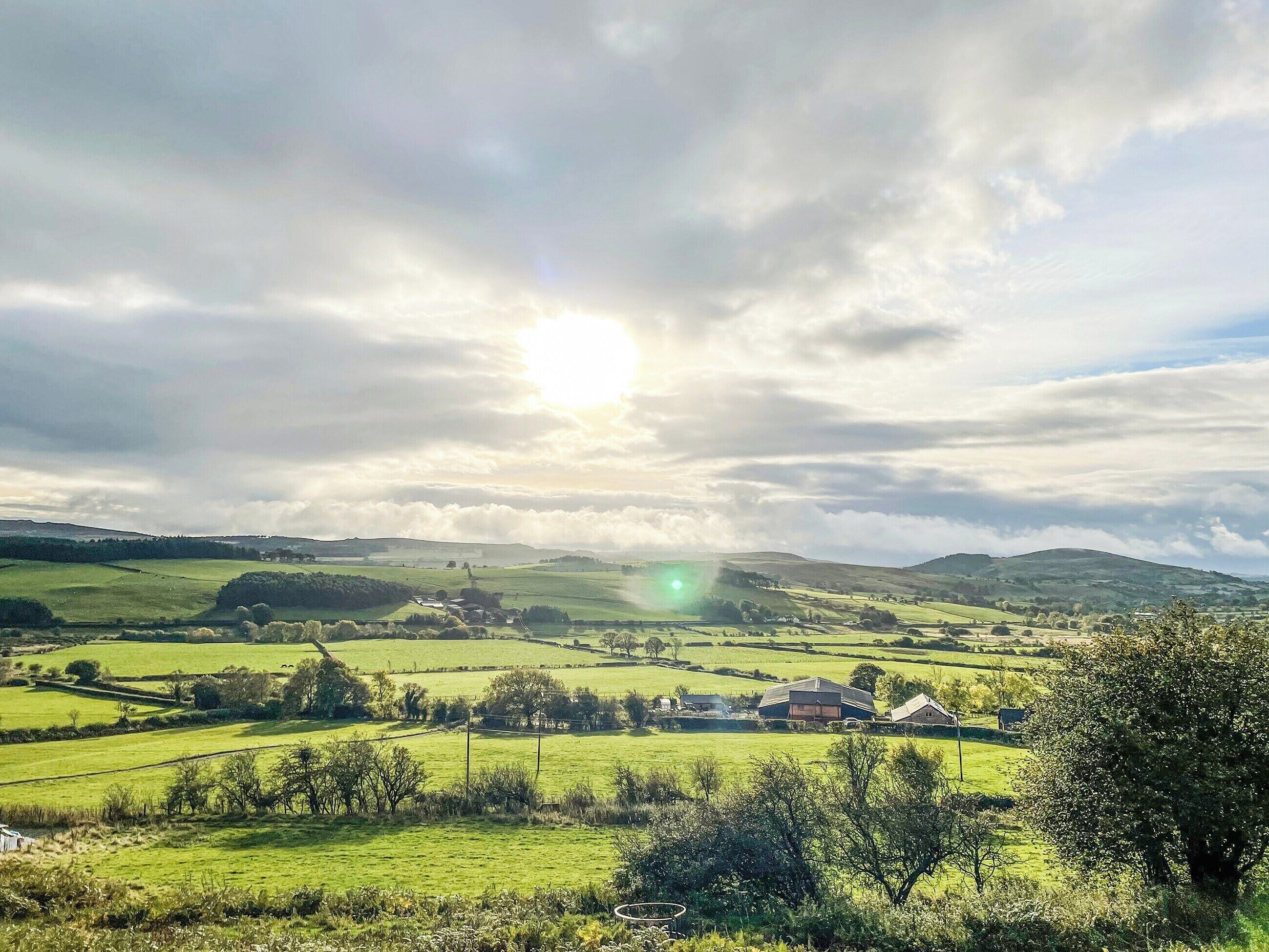 A rural landscape with rolling hills, a small village, and a clear sky.