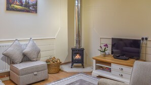 A cozy living room with a fireplace, a sofa, a television, and a painting on the wall. - The Stables at Early Autumn (Sevenoaks)