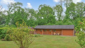 A wooden cabin with a porch, surrounded by a grassy yard and trees. - The Stables at Early Autumn (Sevenoaks)