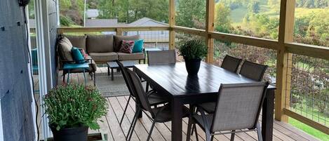A covered outdoor patio with a wooden deck, a dining table with chairs, a sofa, and a fan.