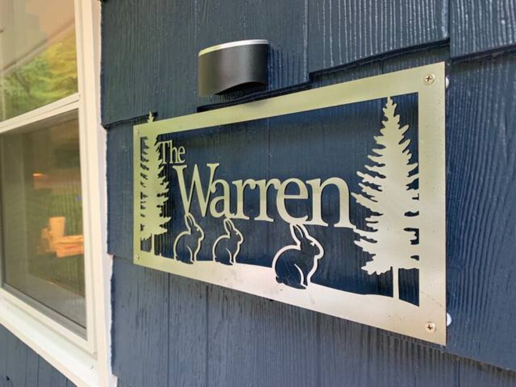 A metal sign with the name 'The Warren' and silhouettes of trees and animals.
