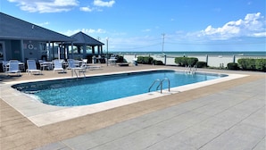 A swimming pool with lounge chairs and a covered seating area, overlooking a body of water.