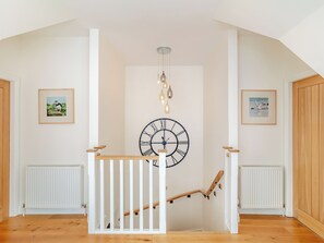 Een trap met een witte leuning, een grote wandklok en ingelijste foto’s aan de muur.