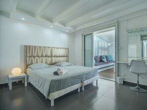 Relax in a serene bedroom with a large bed, bedside table, and comfortable chair, offering a peaceful view from the balcony.