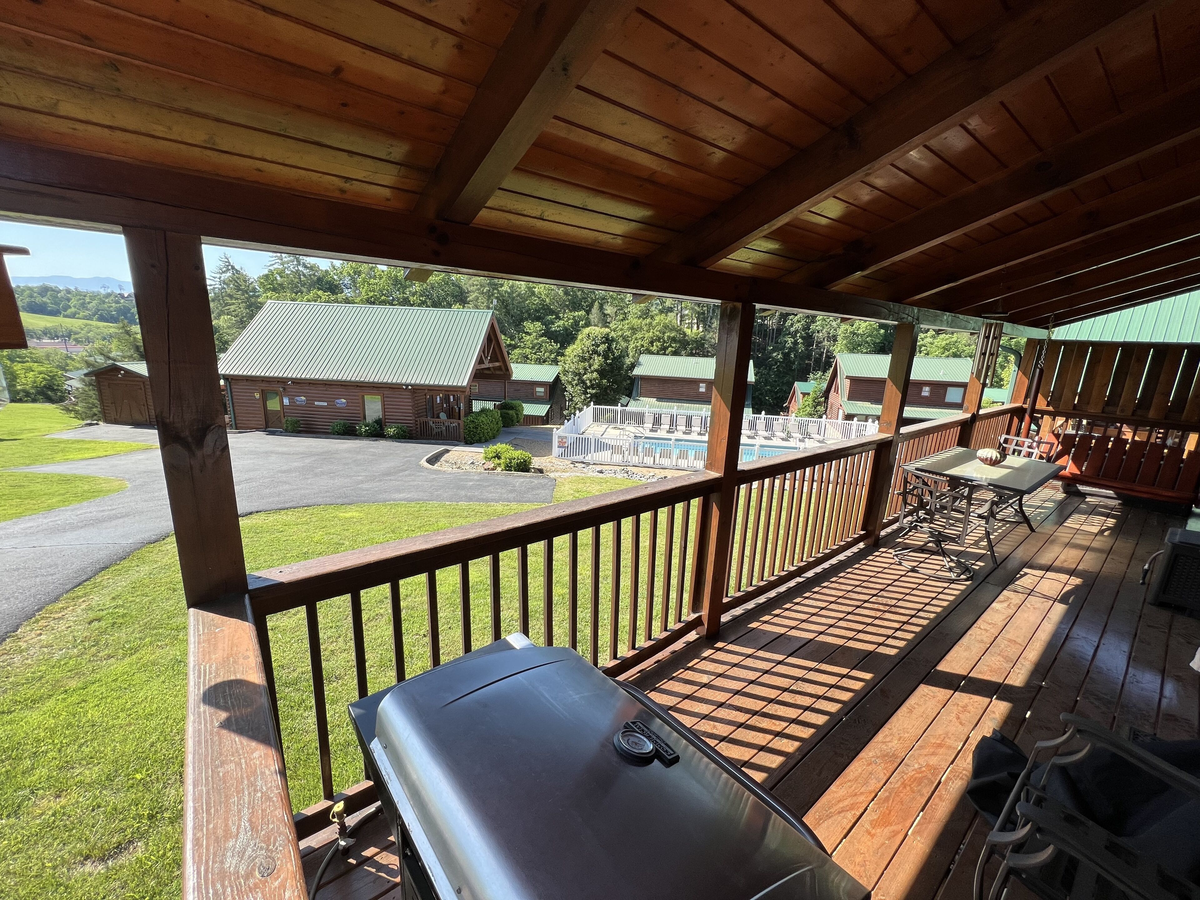 Une terrasse extérieure couverte, équipée d’un barbecue, de rampes en bois et offrant une vue sur un chalet doté d’un toit végétalisé.