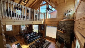 A spacious cabin with a loft bedroom, a fireplace, and a cozy living area with a leather sofa and coffee table. - Beautiful Cabin to Rest & Relax, 1 Mi to Parkway, Hot Tub/Fireplace/Pool/Jacuzzi (Pigeon Forge)