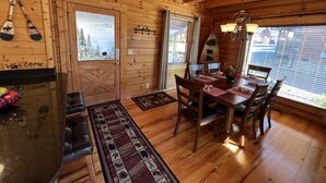 A wooden cabin interior with a dining area, a fireplace, and a view of the outdoors. - Beautiful Cabin to Rest & Relax, 1 Mi to Parkway, Hot Tub/Fireplace/Pool/Jacuzzi (Pigeon Forge)