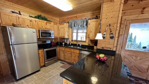 A kitchen with wooden cabinets, stainless steel appliances, a black countertop, and a window with a view of trees. - Beautiful Cabin to Rest & Relax, 1 Mi to Parkway, Hot Tub/Fireplace/Pool/Jacuzzi (Pigeon Forge)