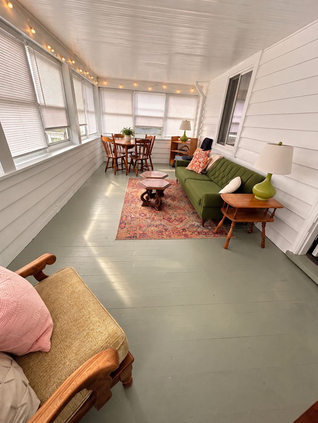 A cozy room with a green sofa, wooden chairs, a small table, and a lamp.