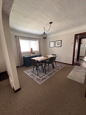 A dining area with a table and chairs, a chandelier, a window with curtains, and a refrigerator in the background. - Comfy Flat with Old World Charm in the city (Jackson)