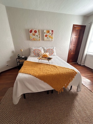 A bedroom with a bed, a nightstand, a lamp, and two wall-mounted paintings. - Comfy Flat with Old World Charm in the city (Jackson)