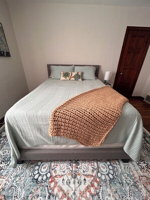 Un lit avec une couvre-lit à motifs, un plaid tricoté et deux coussins ornés de motifs floraux.
