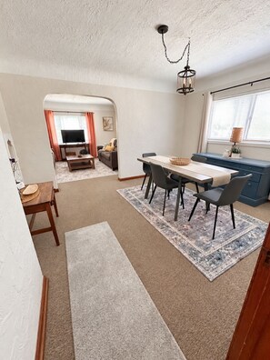 A dining area with a table and chairs, a television in the background, and a kitchen area with a window. - Comfy Flat with Old World Charm in the city (Jackson)