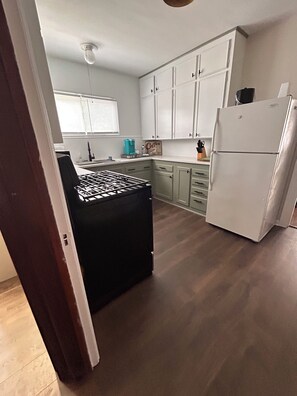 A kitchen with white cabinets, a black countertop, a white refrigerator, and a window with blinds. - Comfy Flat with Old World Charm in the city (Jackson)