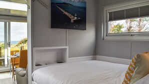 Un dormitorio con cama, un cuadro de un faro, una ventana con persianas y vistas al exterior.