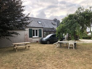 A house with a car parked in the driveway, a picnic table, and a small garden area.