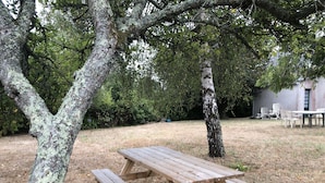Una mesa de picnic con bancos en un área verde con árboles y un edificio al fondo.