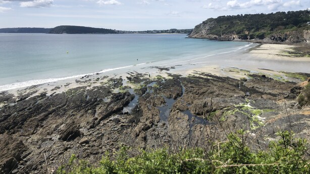 Un paisaje costero con costas rocosas, una playa arenosa y cielo despejado.