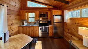 Cocina compacta con paredes de madera, microondas integrado, electrodomésticos de acero inoxidable y un ventanal que proporciona luz natural.