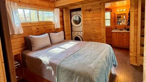 Interior de una cabaña de madera con una cama, lavadora y kitchenette.