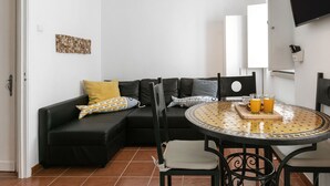 A modern living area with a black leather sofa, a round table with a patterned tablecloth, and two glasses of orange juice. - Casa Casulo - 2min walking to the Beach (Nazaré)