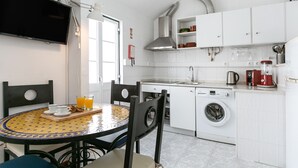 A compact kitchen with a washing machine, a coffee maker, and a dining area with a table and chairs. - Casa Casulo - 2min walking to the Beach (Nazaré)