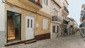 A narrow cobblestone street lined with buildings, a wooden staircase leading to a door marked "CASA CASULO," and a visible fire extinguisher on the balcony. - Casa Casulo - 2min walking to the Beach (Nazaré)