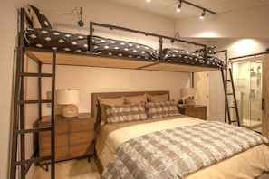 Quarto com beliche, mesa de cabeceira com luminária e área de chuveiro.