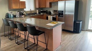 Une cuisine moderne dotée d’un îlot central, de tabourets de bar, d’appareils électroménagers en acier inoxydable et d’armoires en bois.