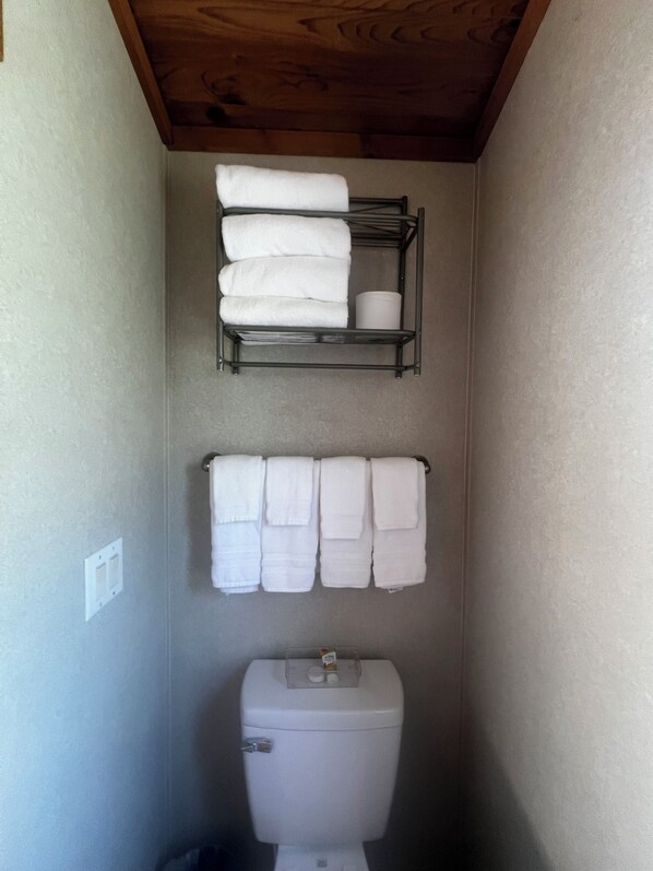 A bathroom with a toilet, a shelf with folded towels, and a wall-mounted towel rack.