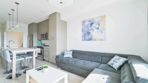 Ein modernes Wohnzimmer mit einer grauen Couch, einem weißen Couchtisch und einer Küchenzeile mit Mikrowelle und Schränken.