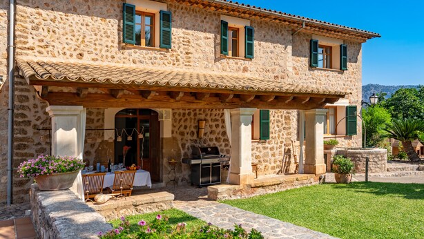A stone building with a tiled roof, green shutters, and a covered patio area with outdoor furniture. - Sa Finqueta Luxury Elegant Mansion with breathtaking views in Sóller (Sóller)