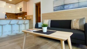 A modern living room with a black sofa, a wooden coffee table, and a kitchen area with white bar stools. - Stylish Friendly Holiday Home (Playa del Inglés)