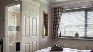 A bedroom with a bed, a window with blinds, a door leading to a bathroom, and a towel rack. - 1 bedroom accommodation in Bridlington (Bridlington)