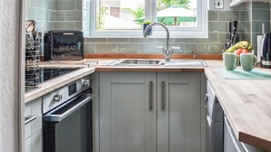 A modern kitchen with grey cabinets, a built-in oven, a sink, and a window with a view of greenery outside. - 1 bedroom accommodation in Bridlington (Bridlington)