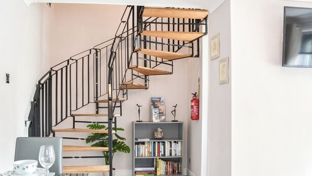 A modern staircase with wooden steps and black metal railings, leading to a landing area with a bookshelf and a fire extinguisher. - 1 bedroom accommodation in Bridlington (Bridlington)