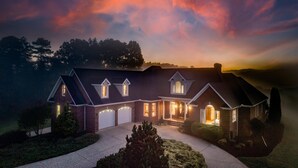 Een groot, twee verdiepingen tellend huis met een bakstenen gevel en meerdere garage deuren, omgeven door een verzorgd gazon en bomen.