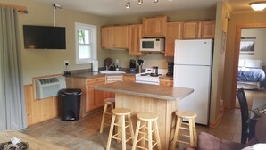 A compact kitchen with wooden cabinets, a microwave, a stove, and a refrigerator. There are three wooden stools at the island.